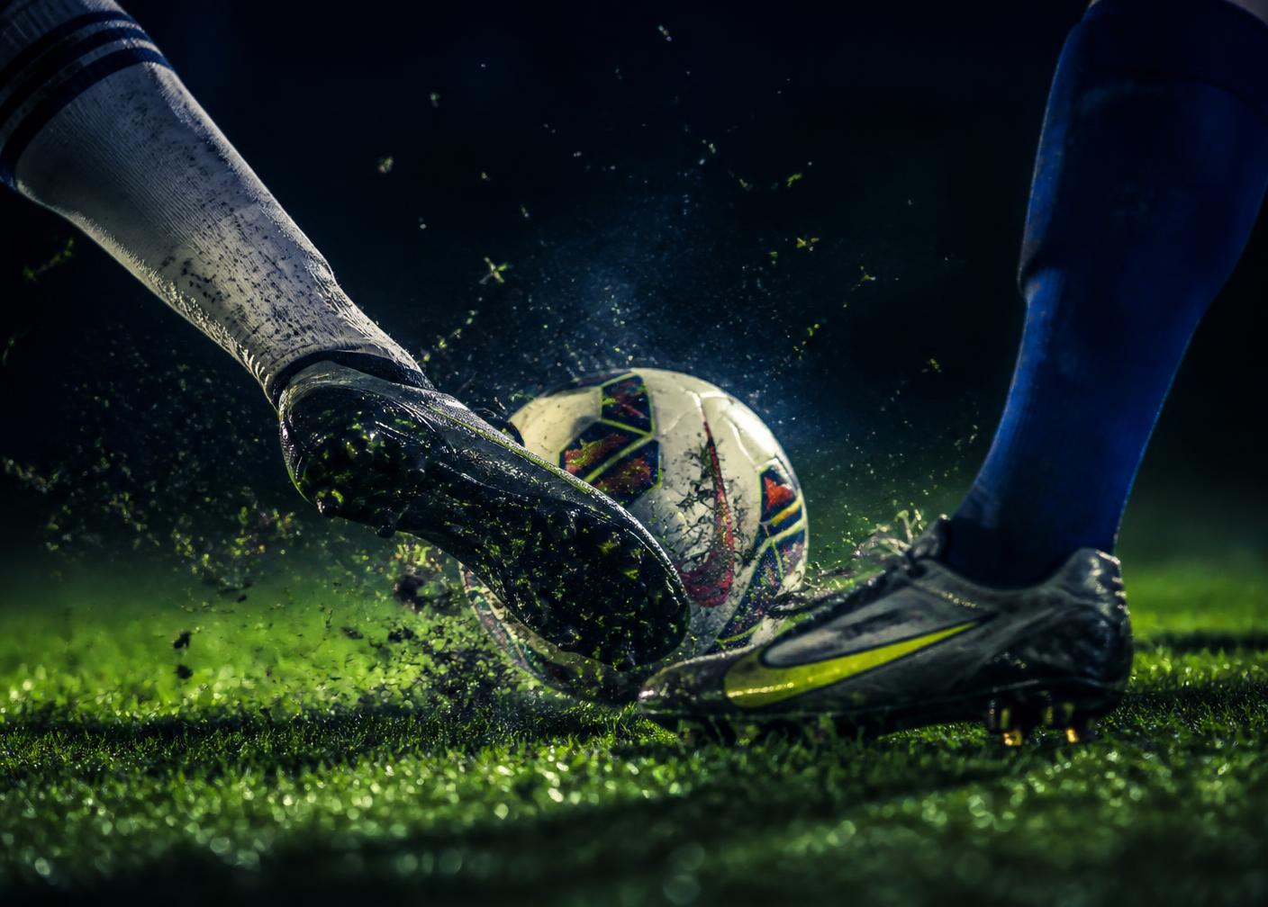 Close-up of boots striking the ball on wet floodlit grass