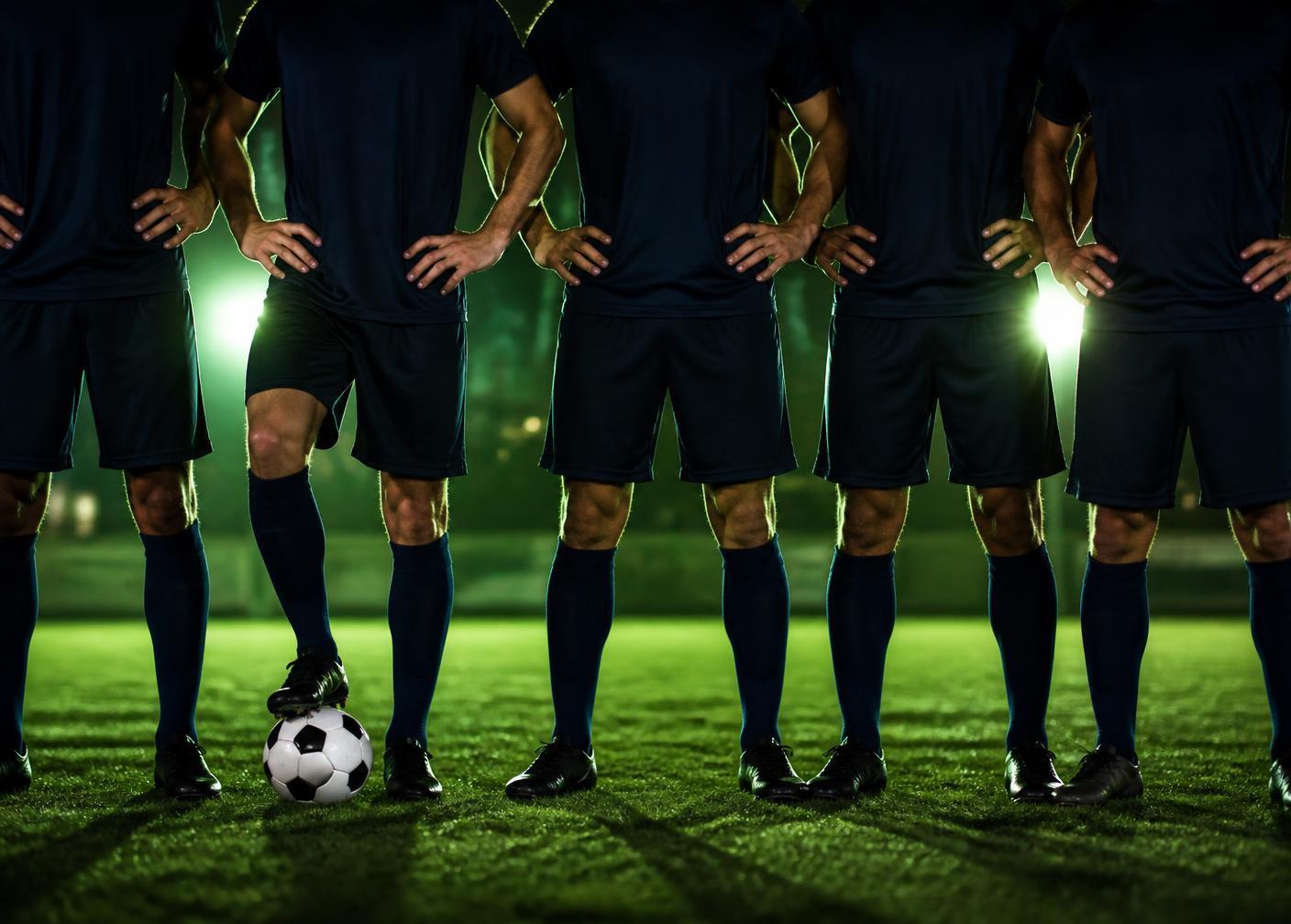 Row of players in navy kit lined up on a floodlit pitch, framed from the chest down